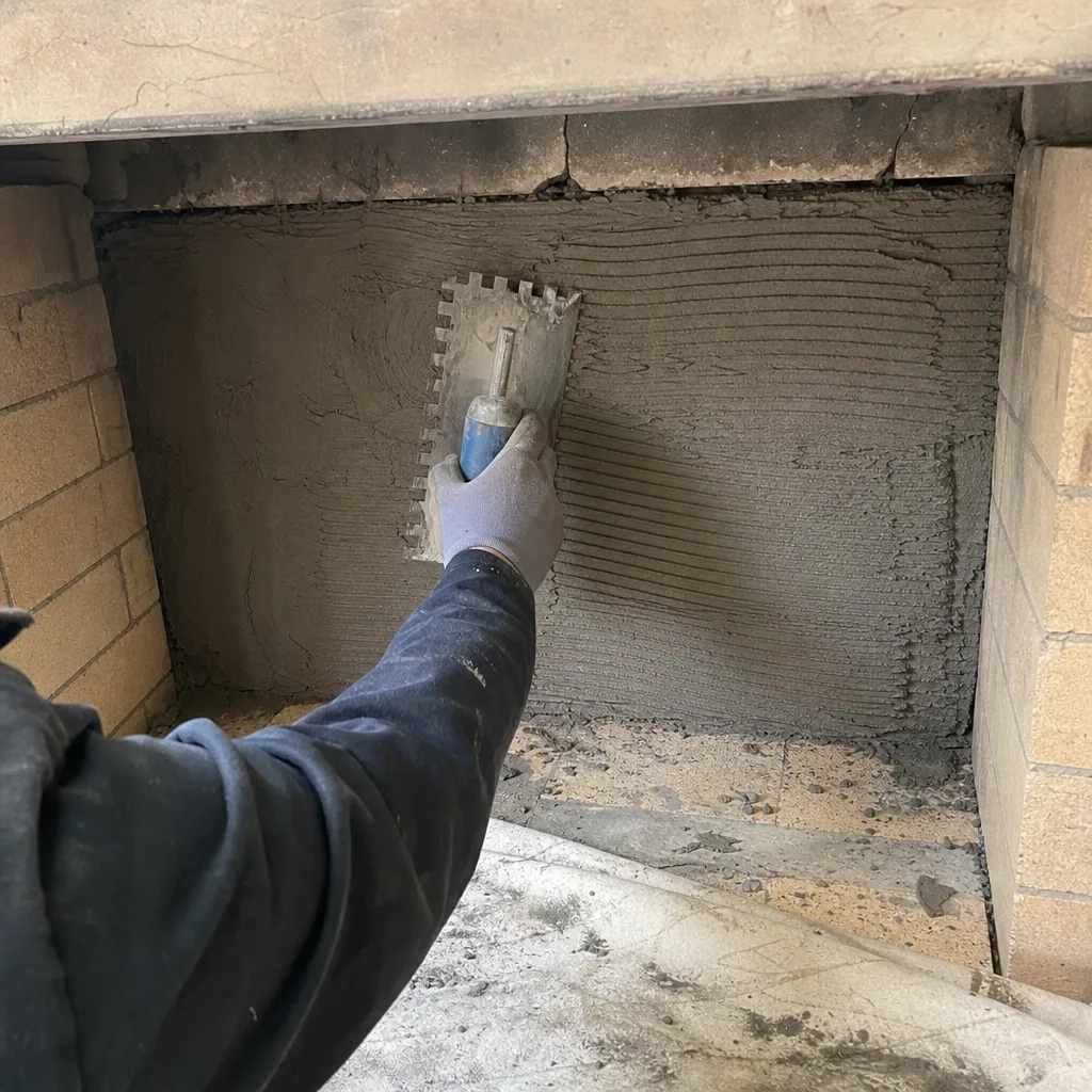 Worker applying mortar to a fireplace firebox with a notched trowel